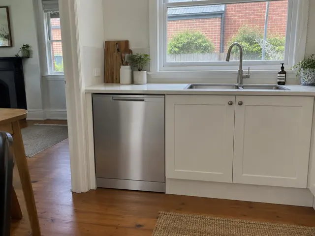 Built-in dishwasher under a kitchen benchtop beside a sink, in a white timber kitchen in Carrington