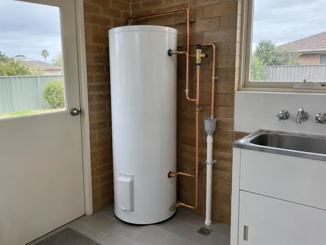 New hot water cylinder beside a laundry sink and brick wall in a home interior in Fern Bay
