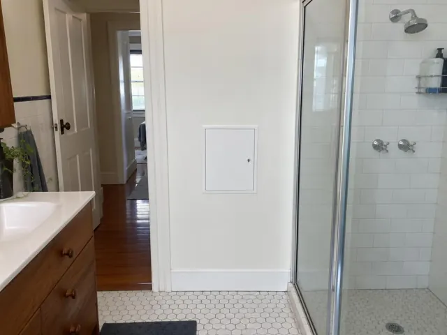 Bathroom wall with a small access panel beside a tiled shower and vanity in Stockton