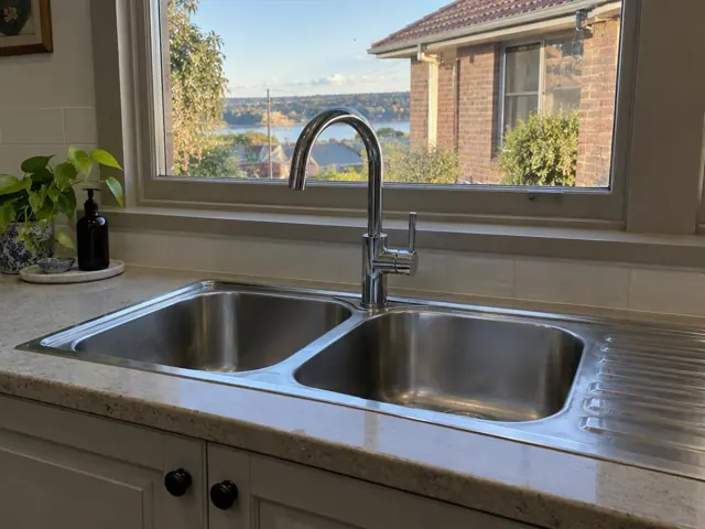 Stainless steel kitchen sink with mixer tap beside a tiled splashback and window in Stockton