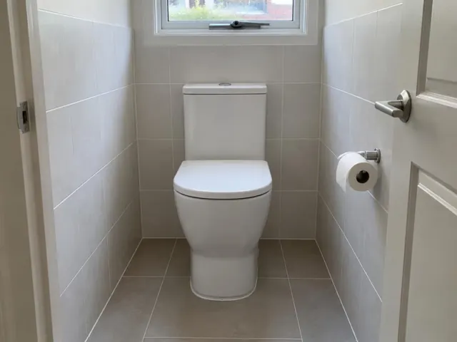 White toilet in a tiled small bathroom with a window above in Newcastle